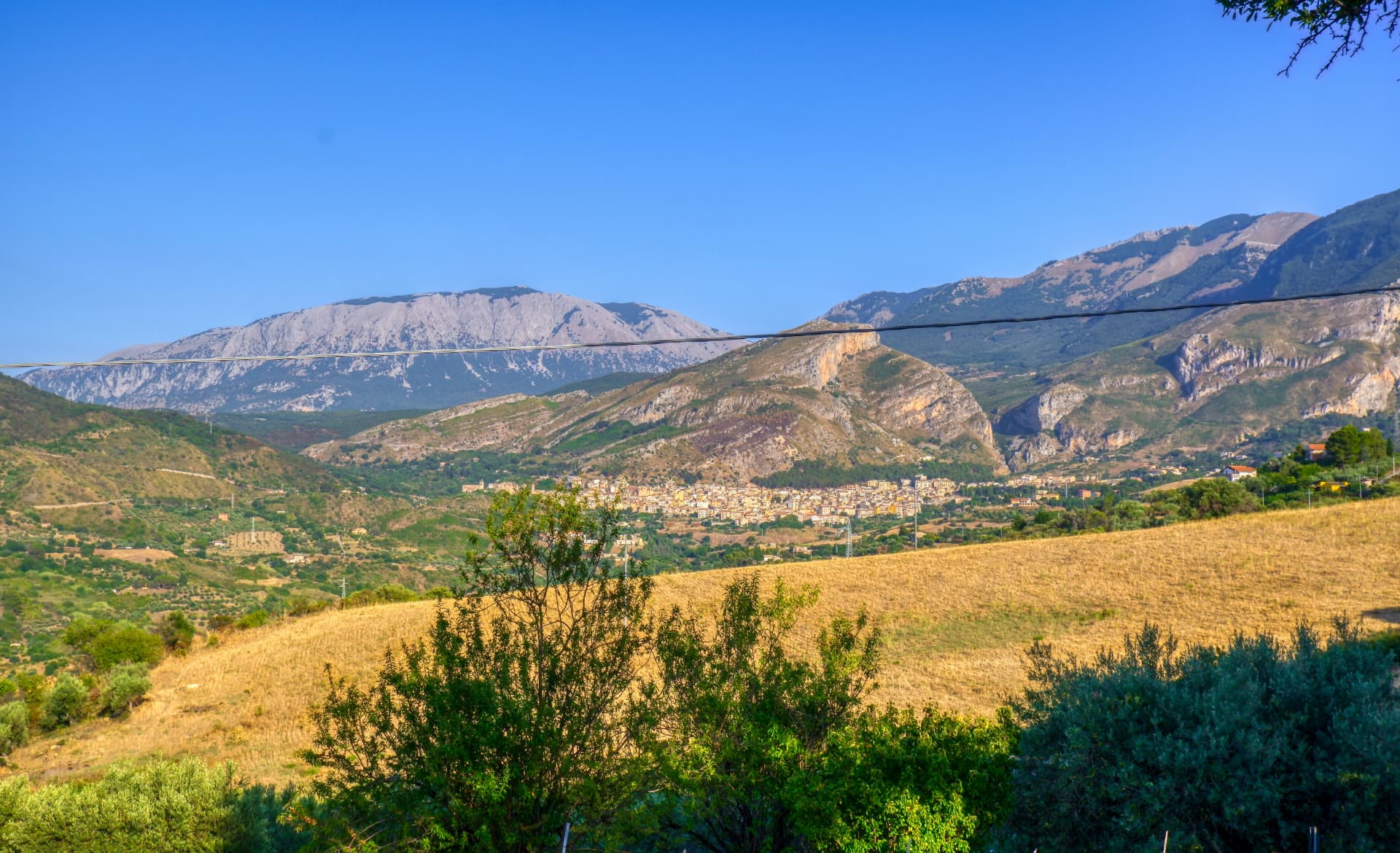 Il borgo di Castelbuono ai piedi delle Madonie, con colline dorate e vette rocciose sotto un cielo limpido