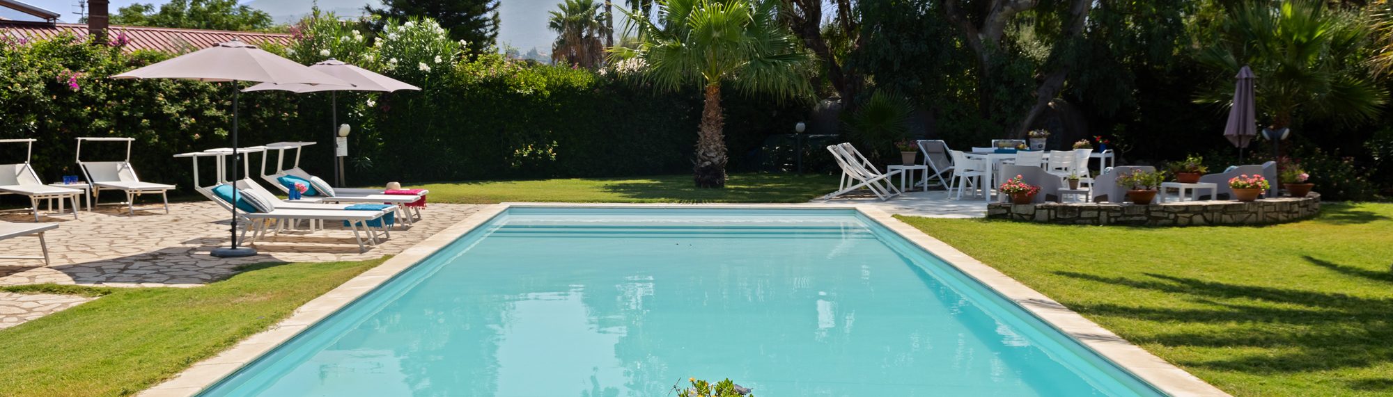 La piscina di Villa Memi con i lettini, il prato e la vegetazione mediterranea